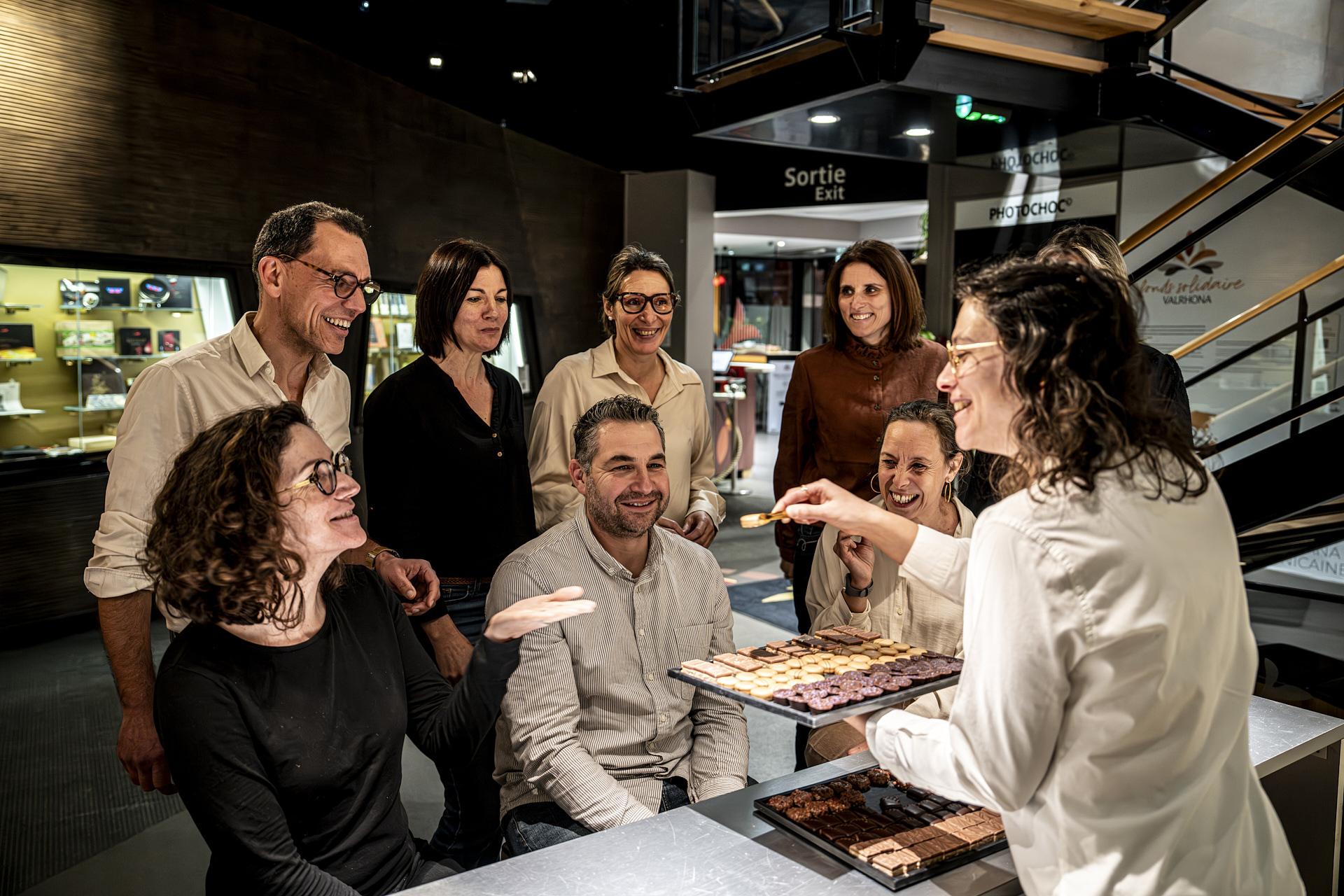 Photographie officielle de visiteurs adultes devant une démonstration de chocolats à la Cité du Chocolat Valrhona.