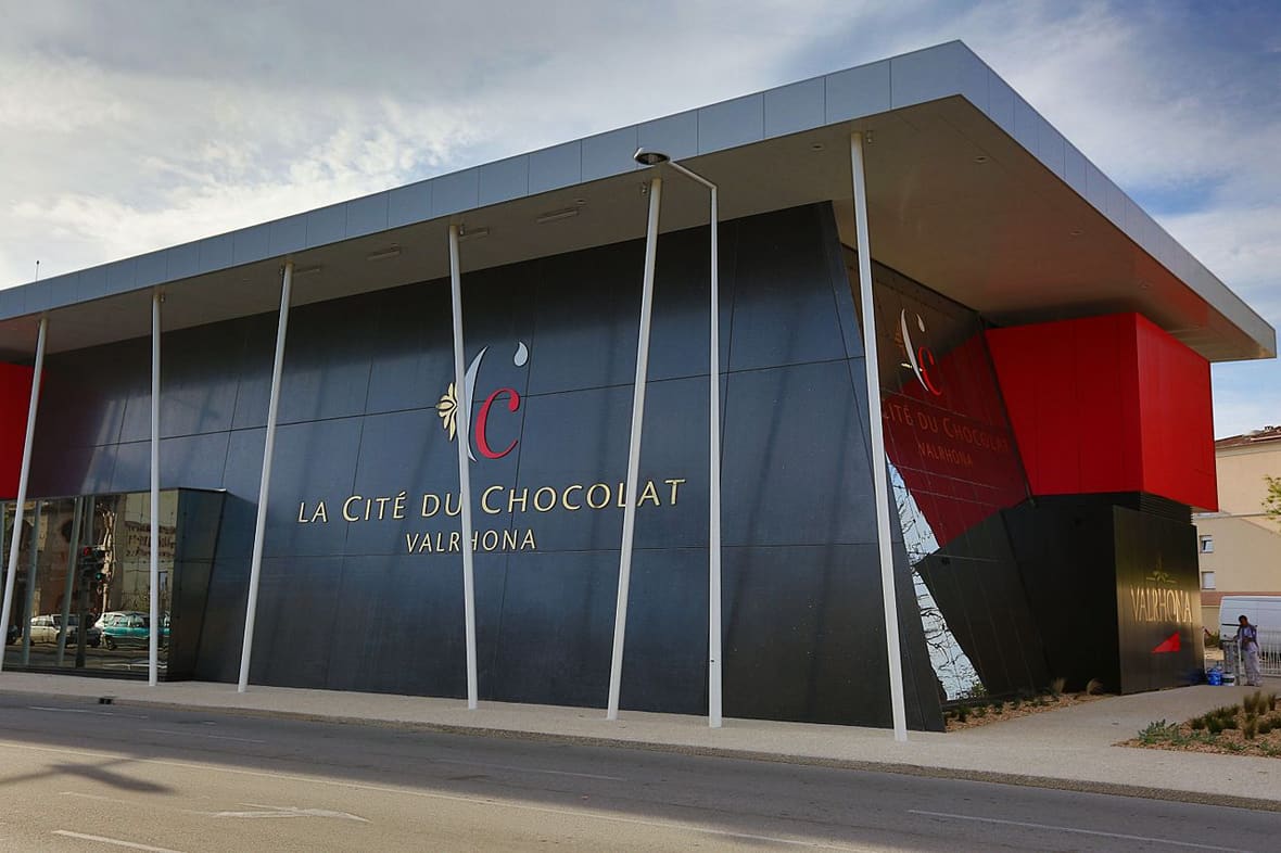 Vue extérieure de la Cité du Chocolat Valrhona, avec sa façade grise et rouge et son enseigne.
